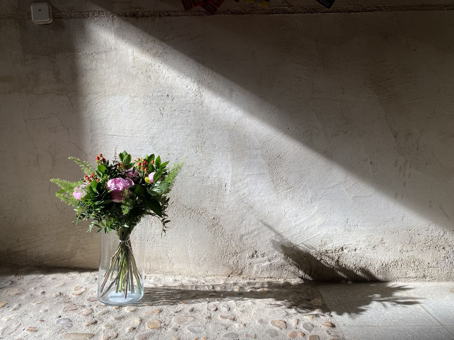 Ramo de flores en jarrón de cristal contra pared de piedra con luz natural